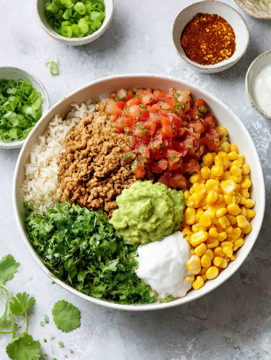 A bowl of food with rice, beans, corn, tomatoes, and guacamole.