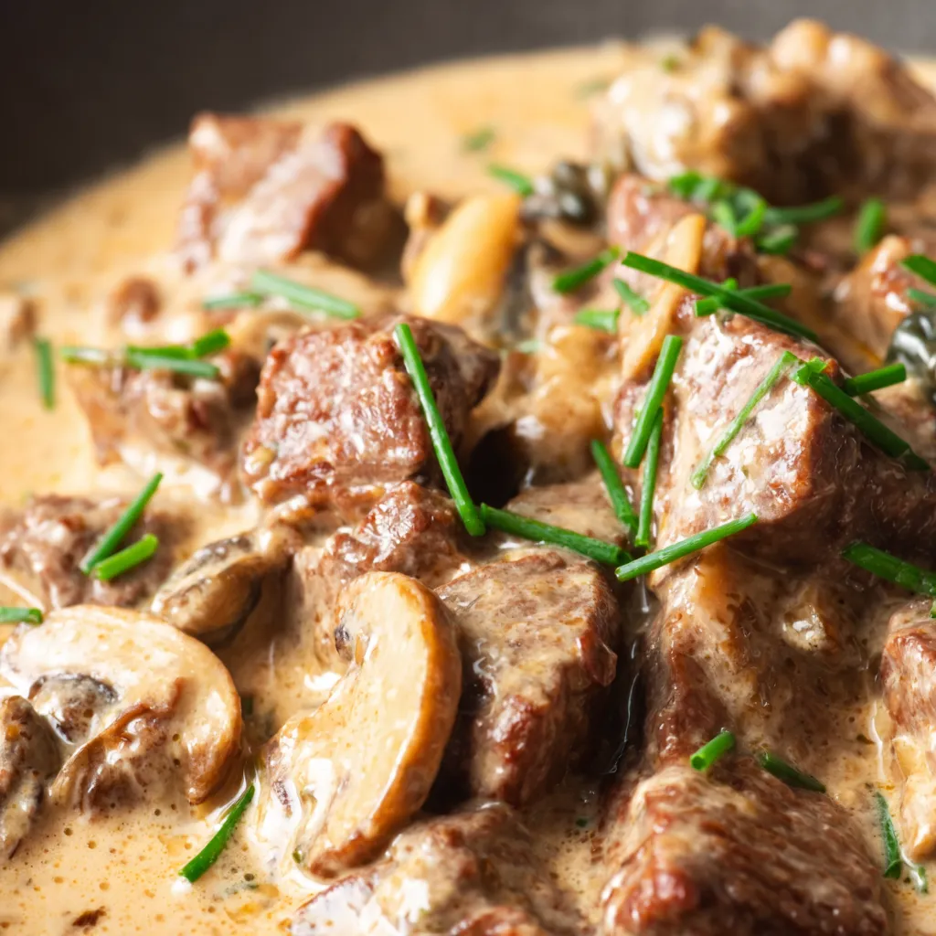 A close up of a beef stew with mushrooms and herbs.