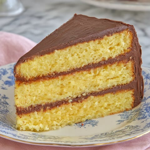 A slice of yellow cake with chocolate frosting.