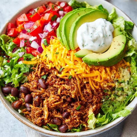 A bowl of food with lettuce, tomatoes, avocado, and sour cream.
