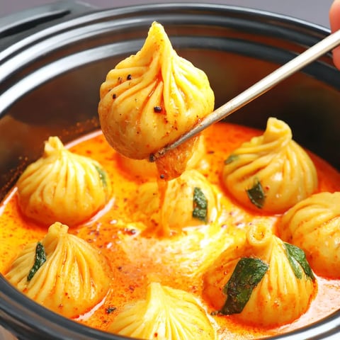 A spoon is in a bowl of soup with dumplings.