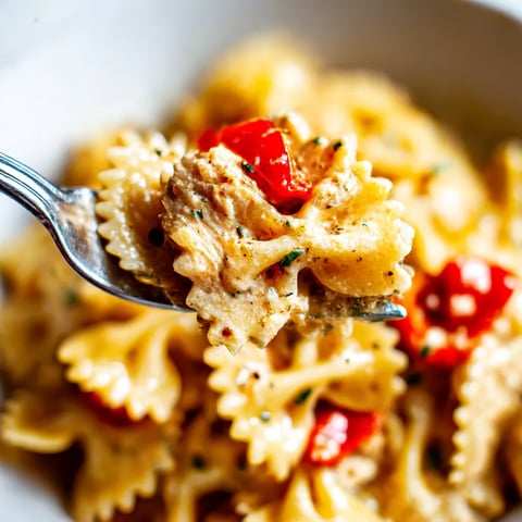 A fork is being used to pick up a piece of pasta with chicken and tomatoes.