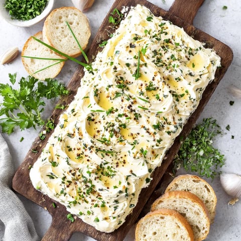 A wooden cutting board with a roasted garlic butter spread on it.