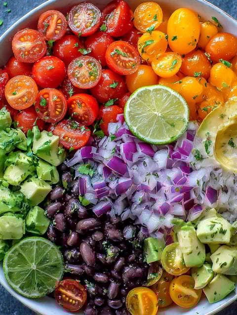 A colorful salad with avocado, lime, black beans, tomatoes, onions, and cilantro.