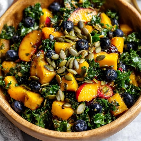 A bowl of salad with blueberries, peaches, and kale.