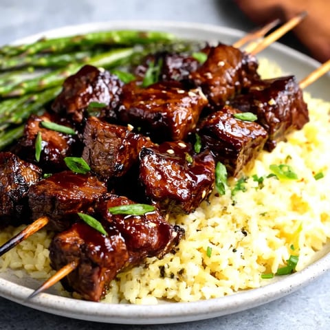 A plate of grilled teriyaki steak kabobs with rice and asparagus.
