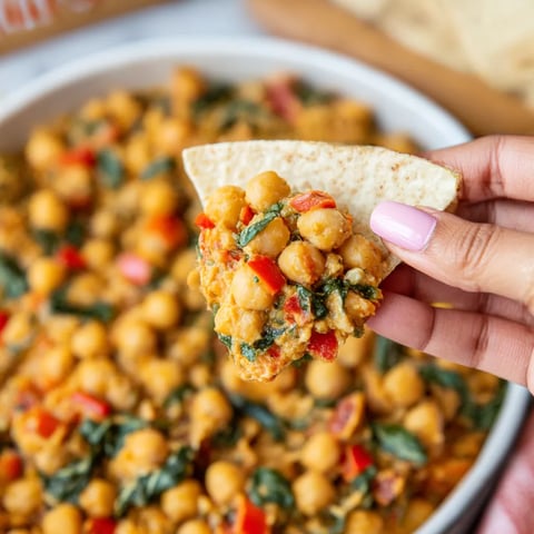 A person is holding a chip with chickpeas on it.